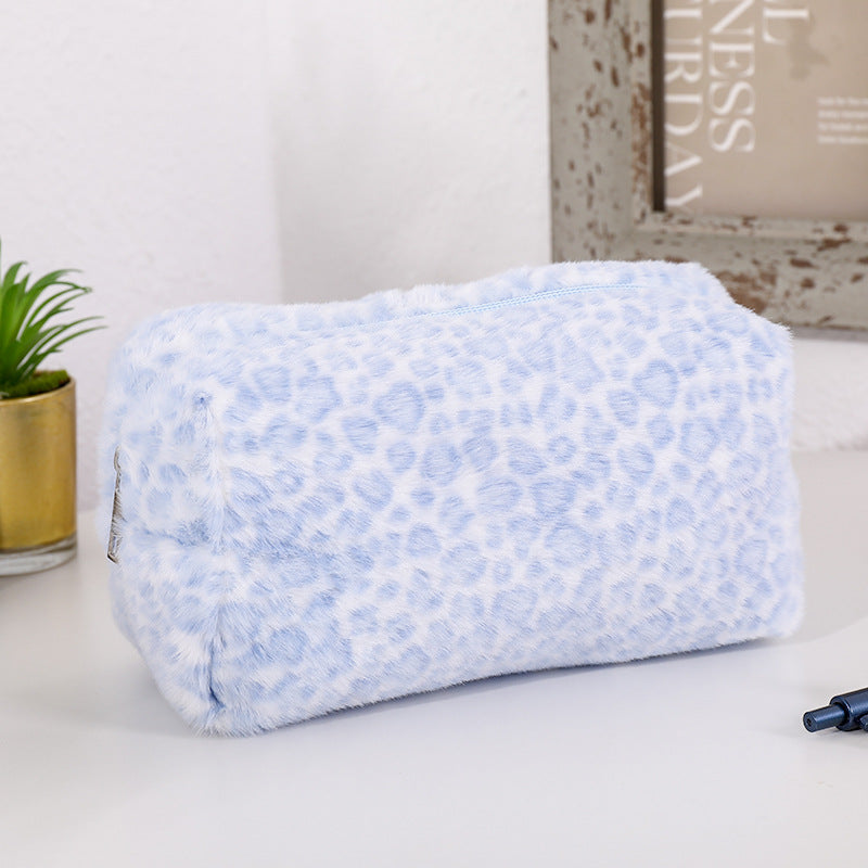 A light blue leopard print cosmetic bag with a plush lining resting on a white surface.