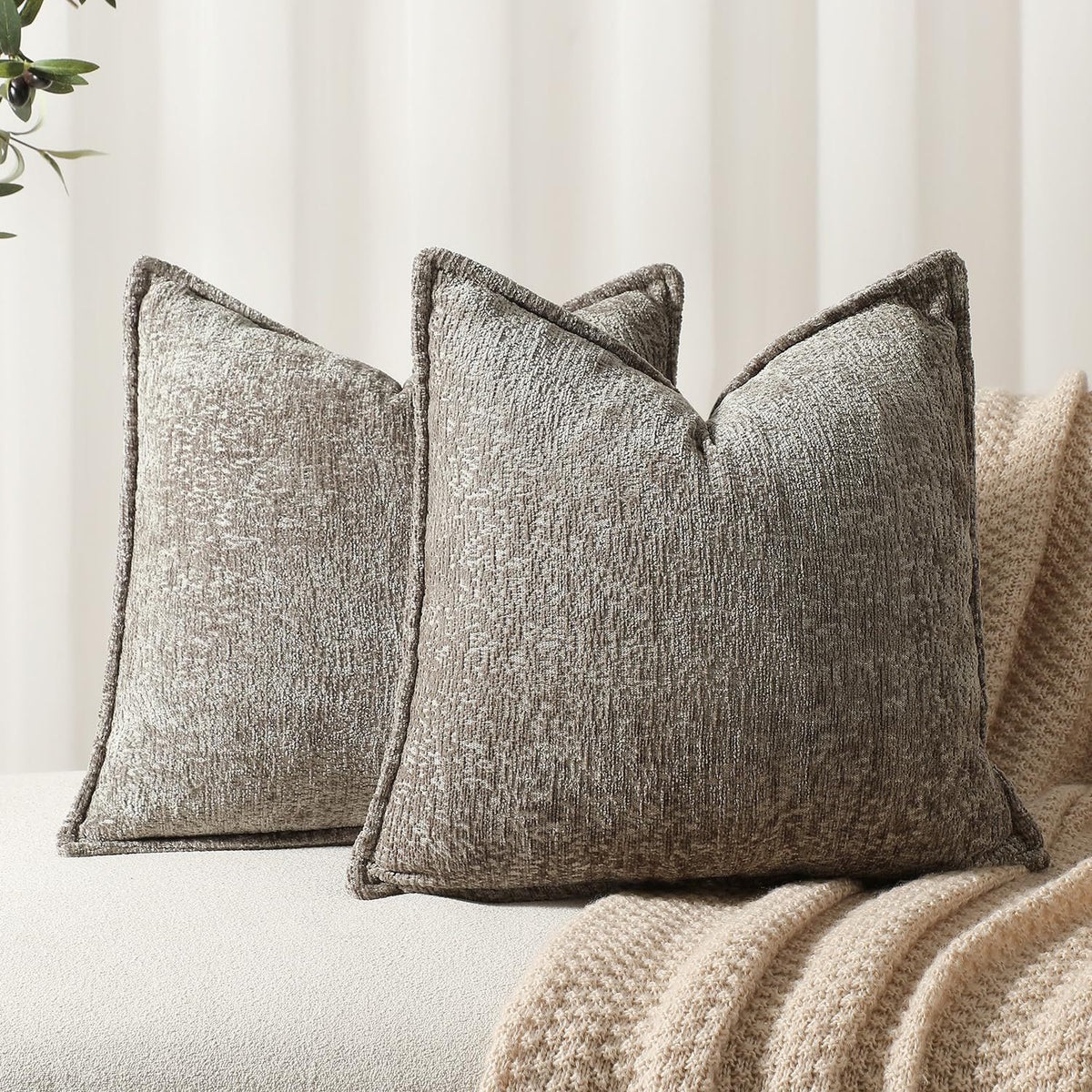 A close-up of a textured gray chenille throw pillow cover resting on a beige knitted blanket.