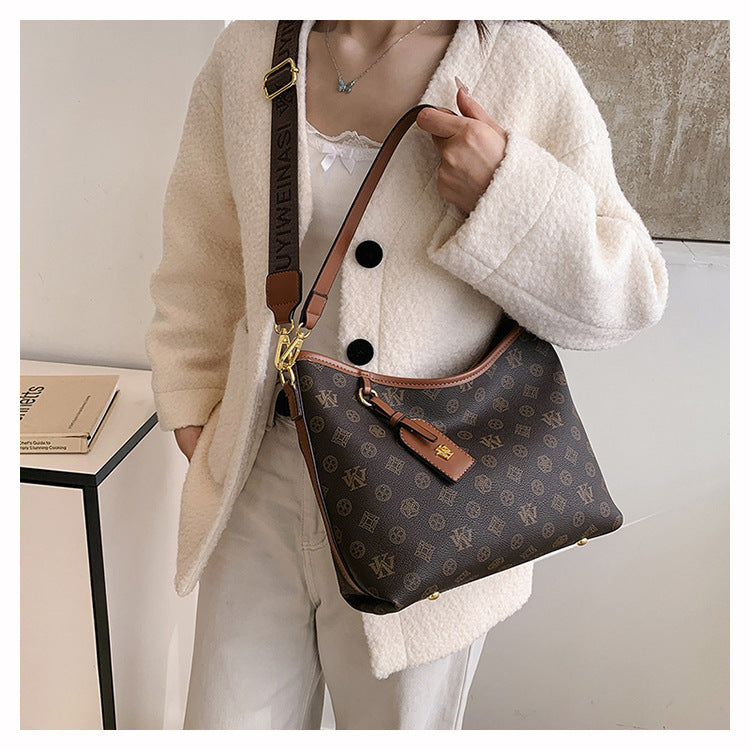 A woman is holding a brown leather tote bag with a gold chain strap and a monogram pattern, worn under a cream-colored jacket