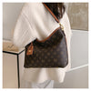 A woman is holding a brown leather tote bag with a gold chain strap and a dark brown patterned fabric against a light colored