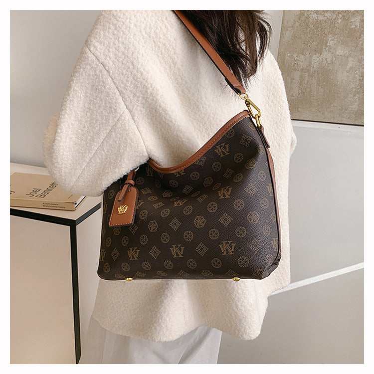 A woman is holding a brown leather tote bag with a gold chain strap and a dark brown patterned fabric against a light colored