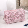 A pink leopard print cosmetic bag with a plush lining resting on a white surface.