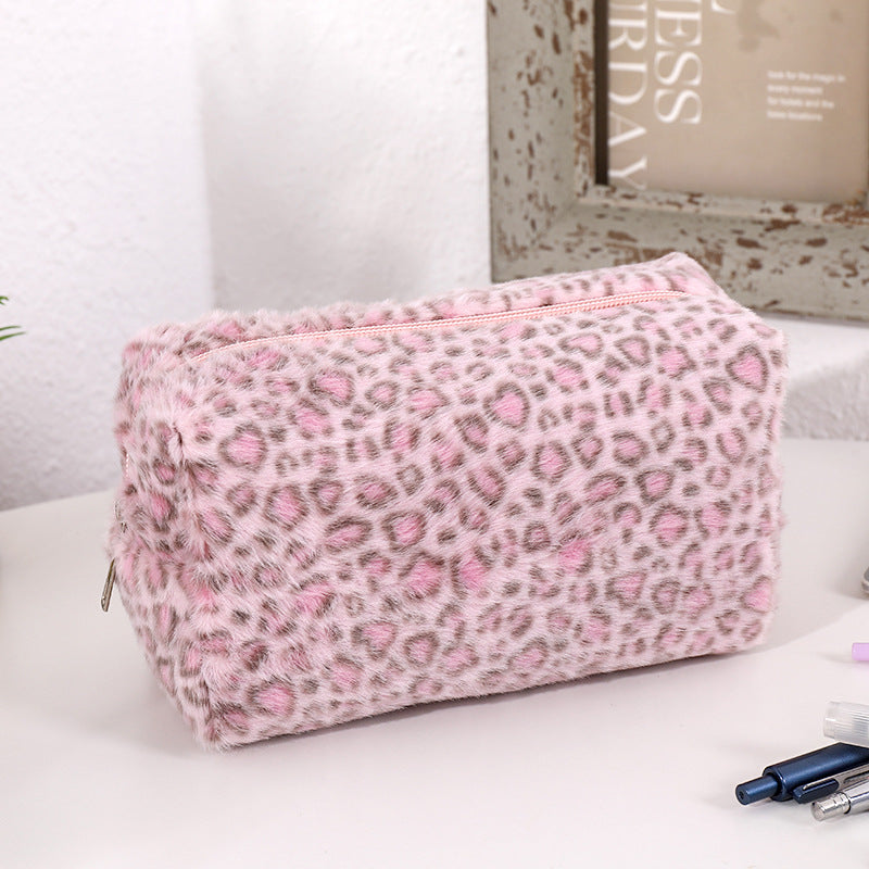 A pink leopard print cosmetic bag with a plush lining resting on a white surface.