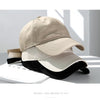 A beige cotton dad hat is shown resting on a white surface with shadows cast by sunlight.