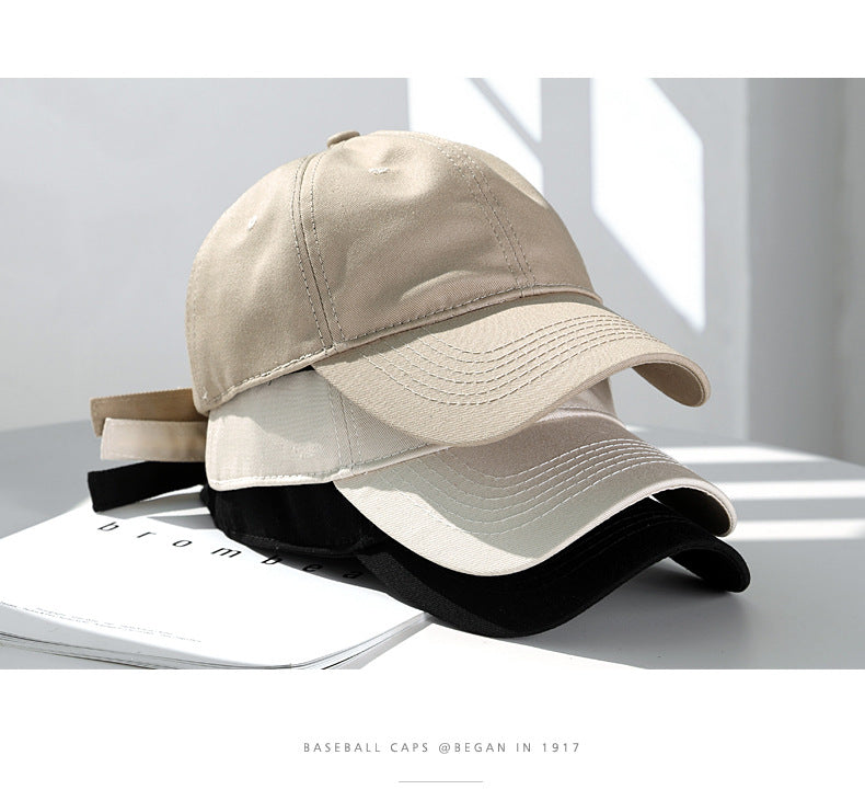 A beige cotton dad hat is shown resting on a white surface with shadows cast by sunlight.