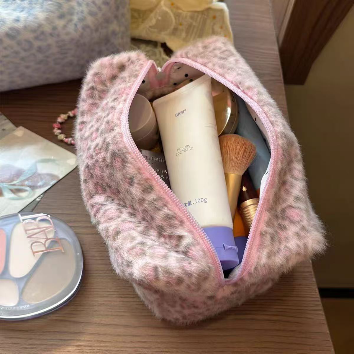 A pink leopard print cosmetic bag with a plush lining is open, revealing makeup products inside.