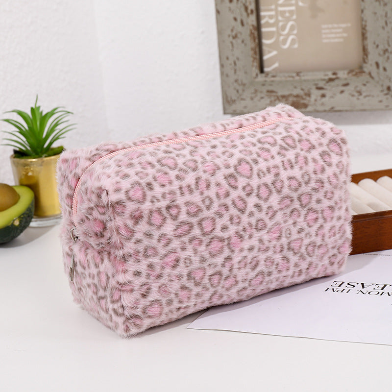 A pink leopard print cosmetic bag with a plush lining resting on a white surface.