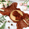 A rust brown cotton gauze table runner draped over a wooden plate on a white rustic surface.