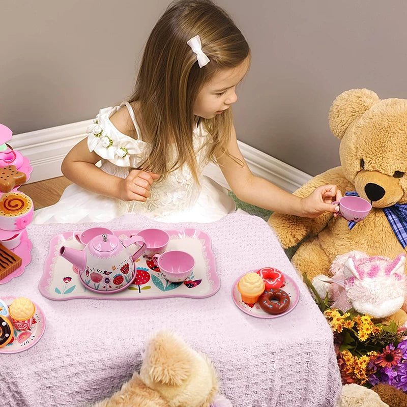 A young girl is playing with a pink pretend play tea set and serving tray on a pink tablecloth.