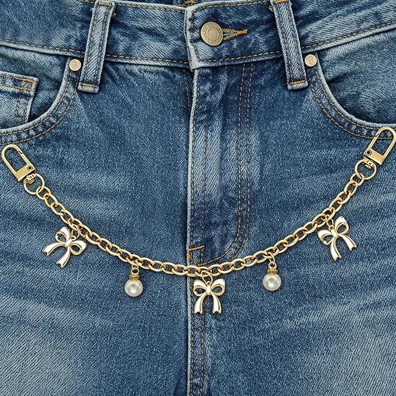 A close-up of a denim jean pocket featuring a gold alloy chain with pearl charms.