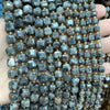 A close-up of natural stone square faceted beads in various shades of gray and brown stacked on a hand.