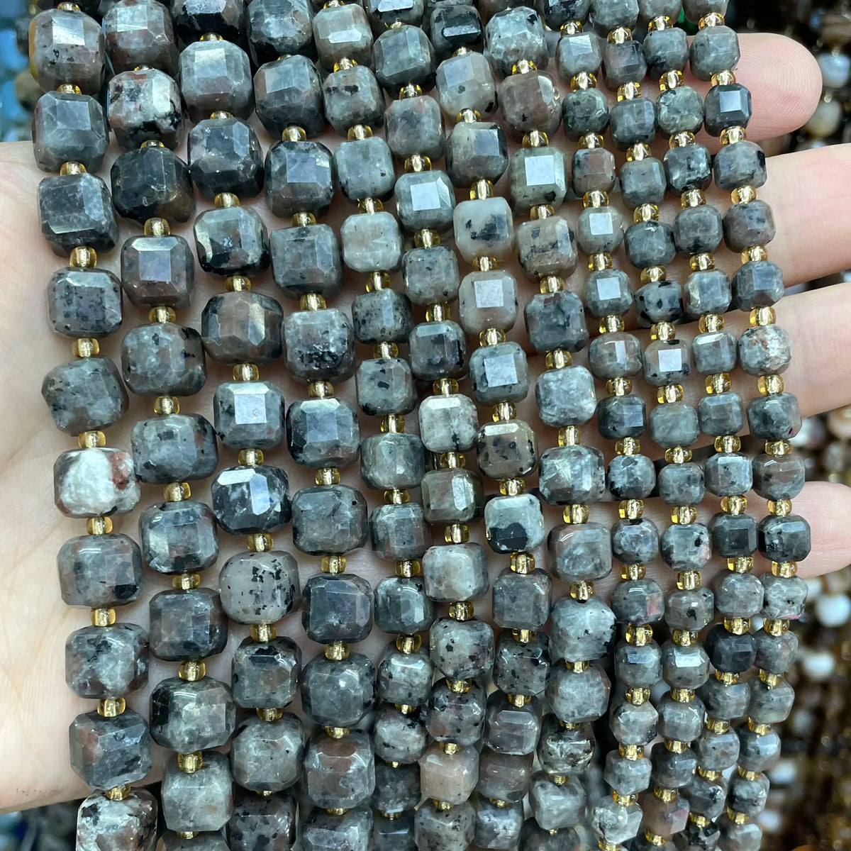 A close-up of natural stone square faceted beads in various shades of gray and brown stacked on a hand.