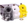 Three fluffy angel bunny keychains in gray, white, and yellow with pom pom tails displayed on a dark box.