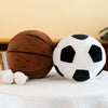 A brown basketball plush toy and a black and white soccer ball plush toy resting on a white cloth.