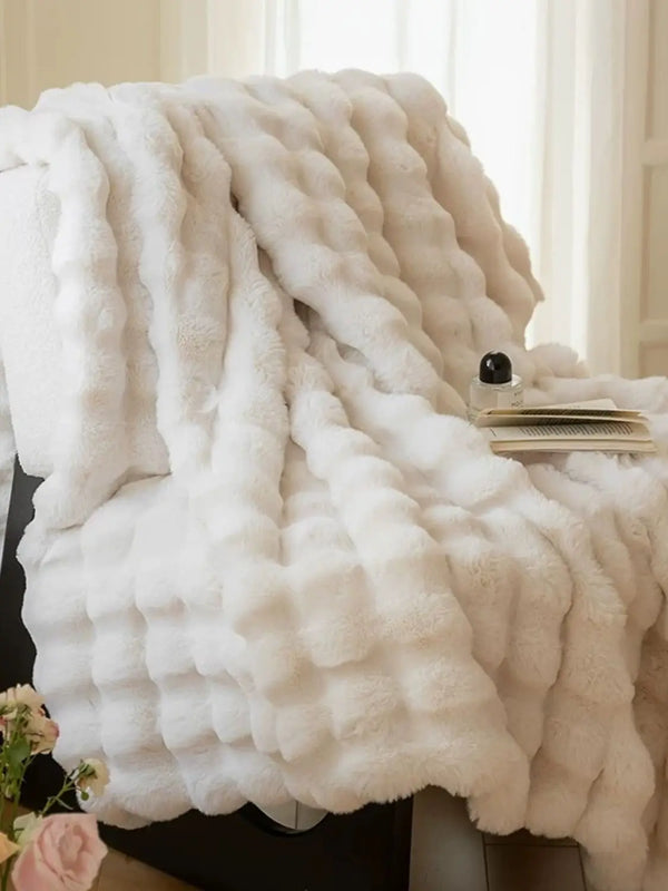 A fluffy white faux rabbit fleece blanket draped over a surface.