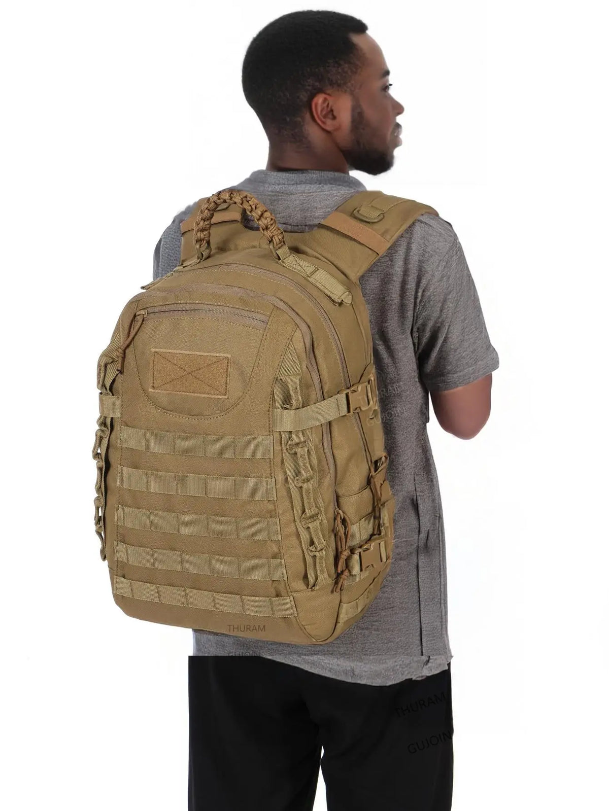 A man is wearing a tan tactical backpack with a MOLLE system and a gray t-shirt.