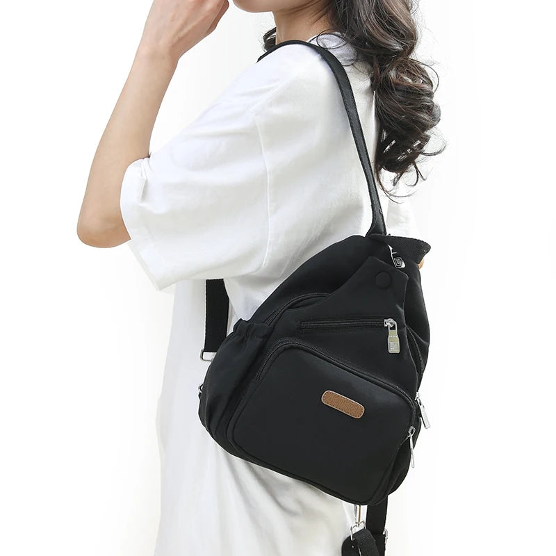 A woman is holding a black waterproof nylon crossbody sling bag against a white top.