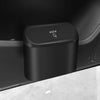 A black portable car trash bin with a push-type lid is shown on a light surface.