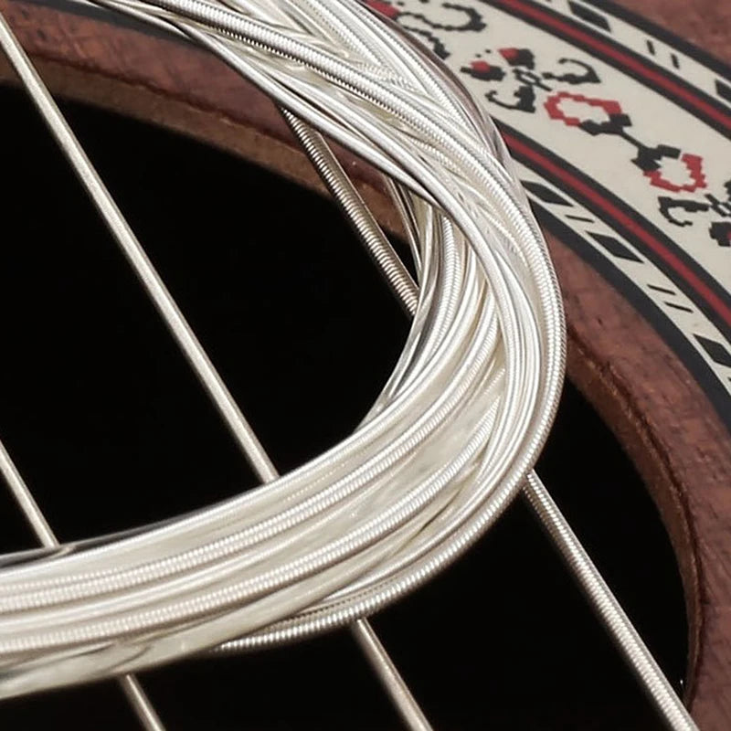 Close-up of silver guitar strings coiled around a wooden fretboard with decorative inlay.
