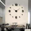 A modern wall clock with black numbers and hands is mounted on a white wall above a glass table.