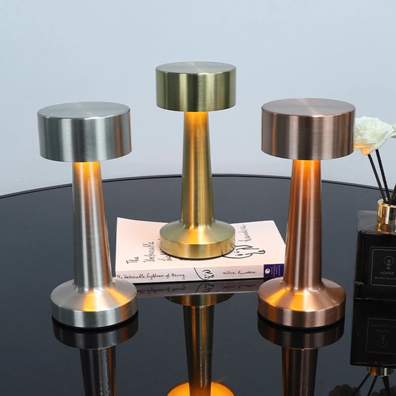 Three rechargeable metal LED table lamps in silver and gold finishes displayed on a reflective surface.