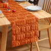 Orange textured table runner with pumpkin designs set on a wooden table.