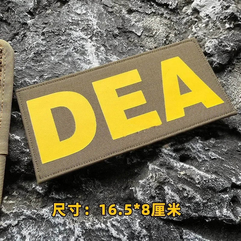 A yellow DEA embroidered patch is displayed on a dark, rough stone surface.