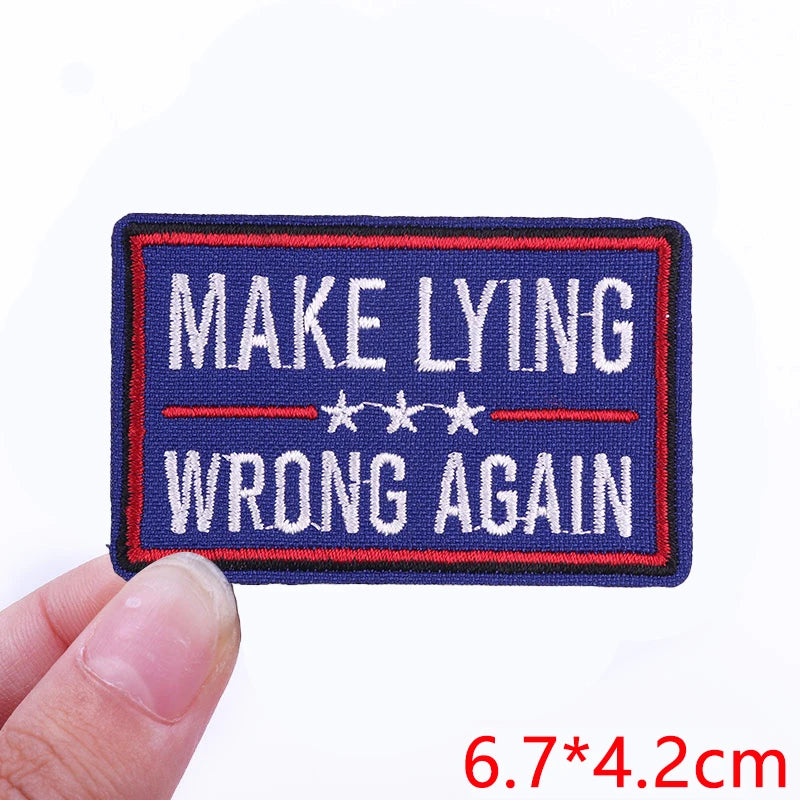 A dark blue embroidered iron-on letter patch with red and white text that reads MAKE LYING WRONG AGAIN
