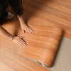 A person's hands are touching a piece of self-adhesive wood grain wallpaper, showing its texture and thickness.