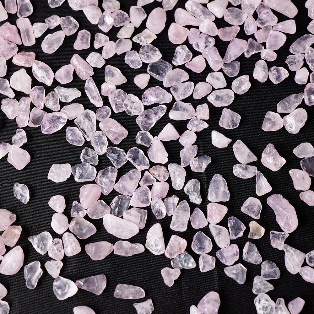 A pile of translucent pink rose quartz crystal gravel scattered on a dark surface.