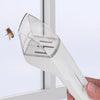 A hand holds a white handheld insect catcher with a telescopic handle, positioned near a window.