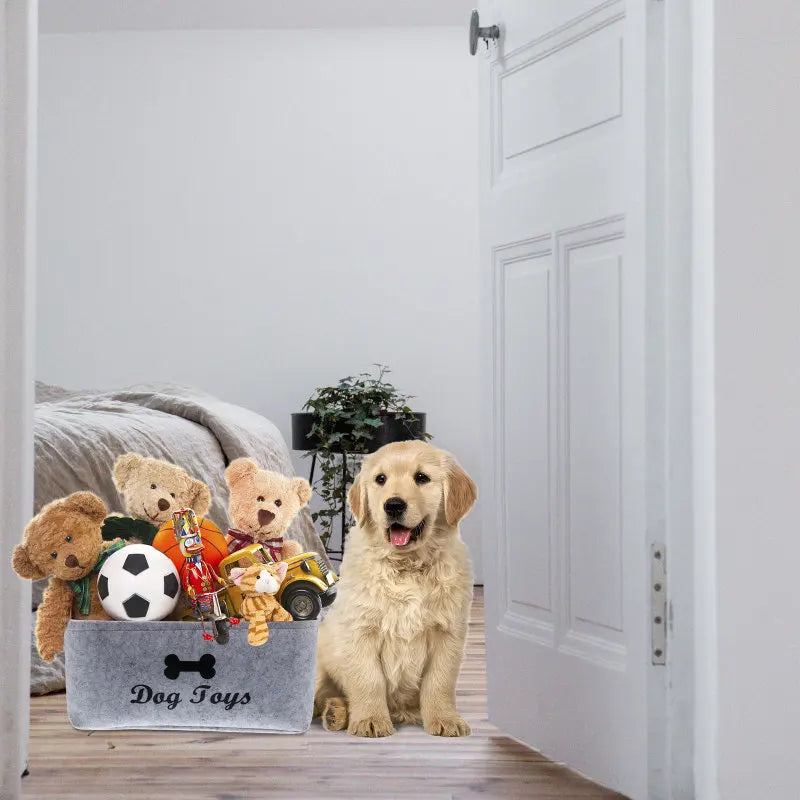 A grey storage basket with wooden handles filled with various felt pet toys including teddy bears and a soccer ball.