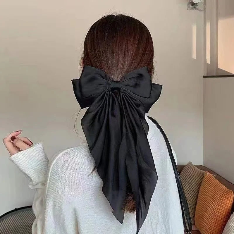 A woman's back shows a black silk bow tied in her hair, with a white sweater visible.