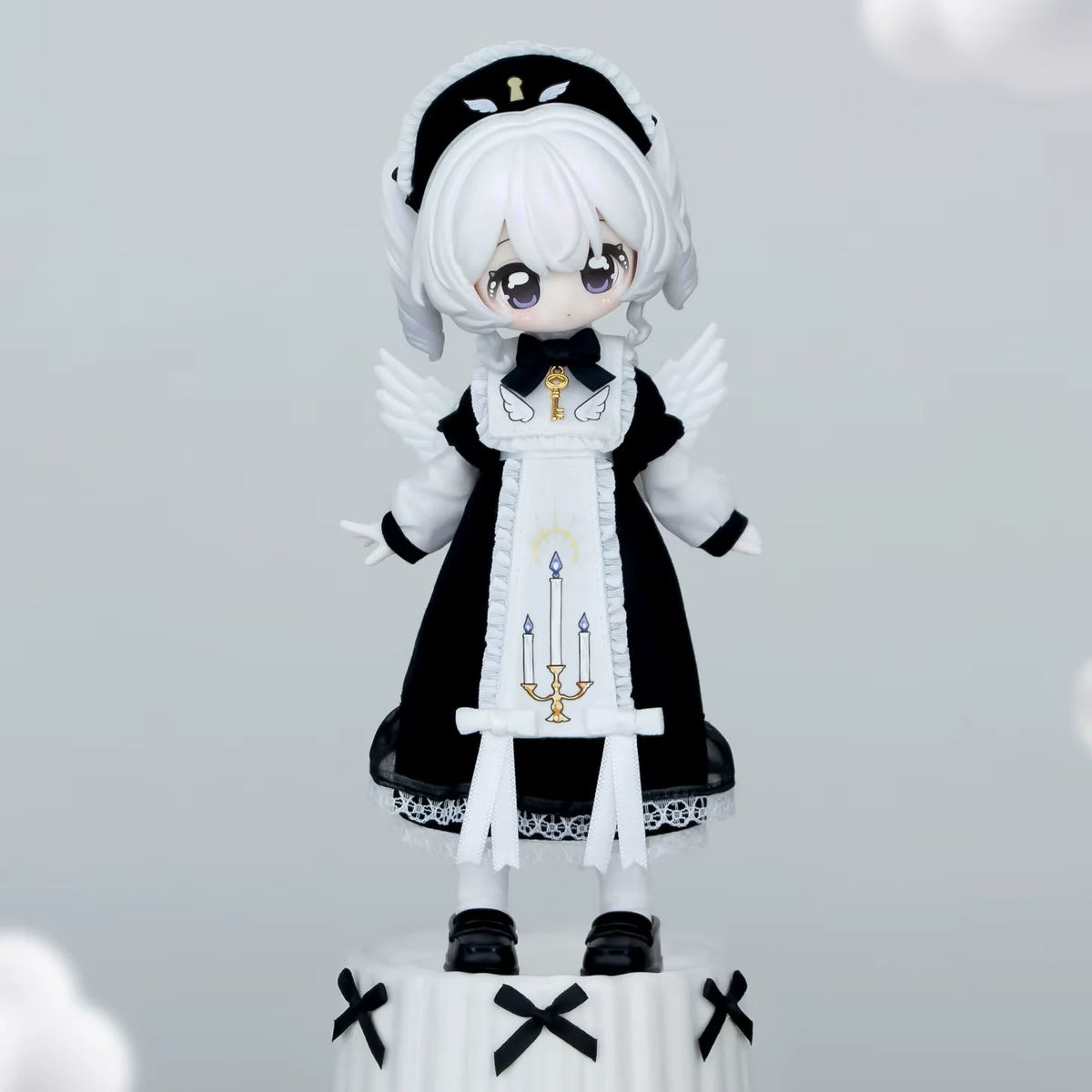 A white-haired doll figurine dressed in a black and white gothic outfit with a hood and wings.