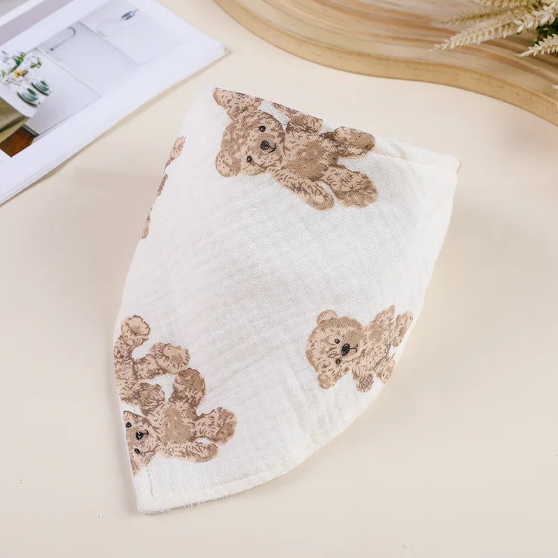 A white cotton baby bib with brown teddy bear print lying on a light surface.