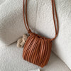A brown pleated faux leather crossbody bag hanging on a light textured surface next to a small teddy bear.