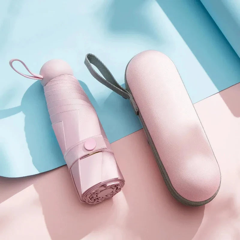 A pink compact 5-fold travel umbrella with a gray strap is shown against a light blue background.