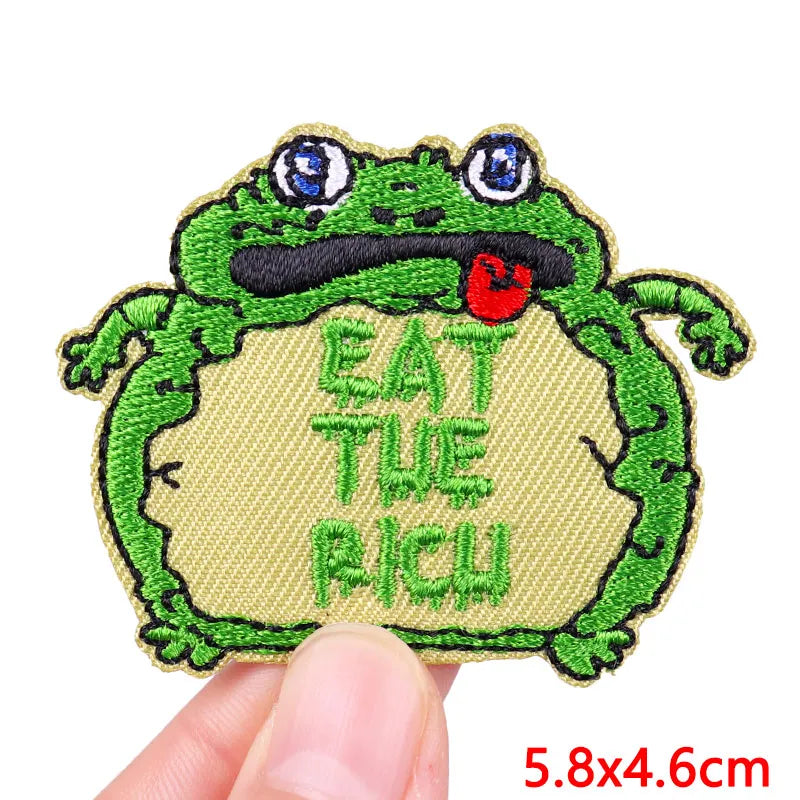 An embroidered patch featuring a green cartoon frog with a red tongue, with the text Eat The Rich.