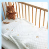 A white quilted baby pillow with a breathable ice silk cover is shown on a wooden crib railing.