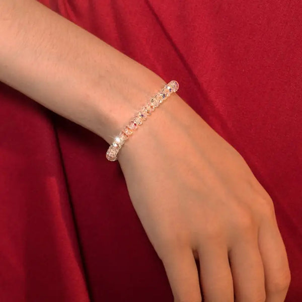 A close-up of a clear crystal bead bracelet worn on a wrist against a red fabric background.