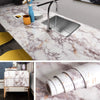 A kitchen sink installed in a marble countertop, with a roll of pearlescent pink marble peel and stick wallpaper nearby.