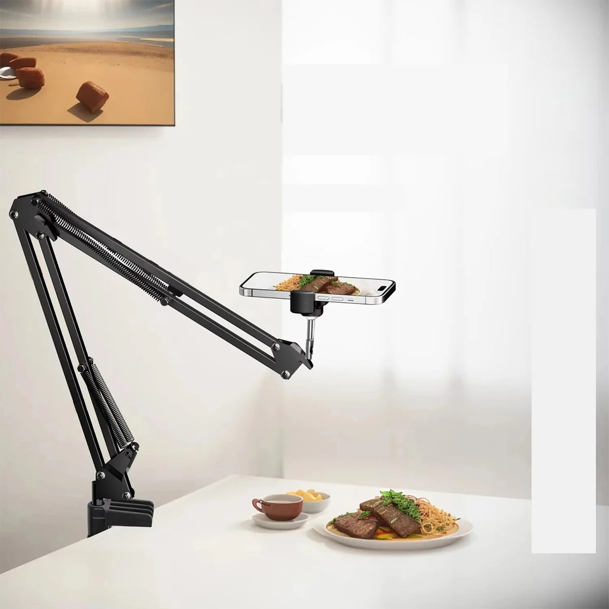 A black adjustable phone stand with an overhead light is positioned above a white table, next to a plate of food.