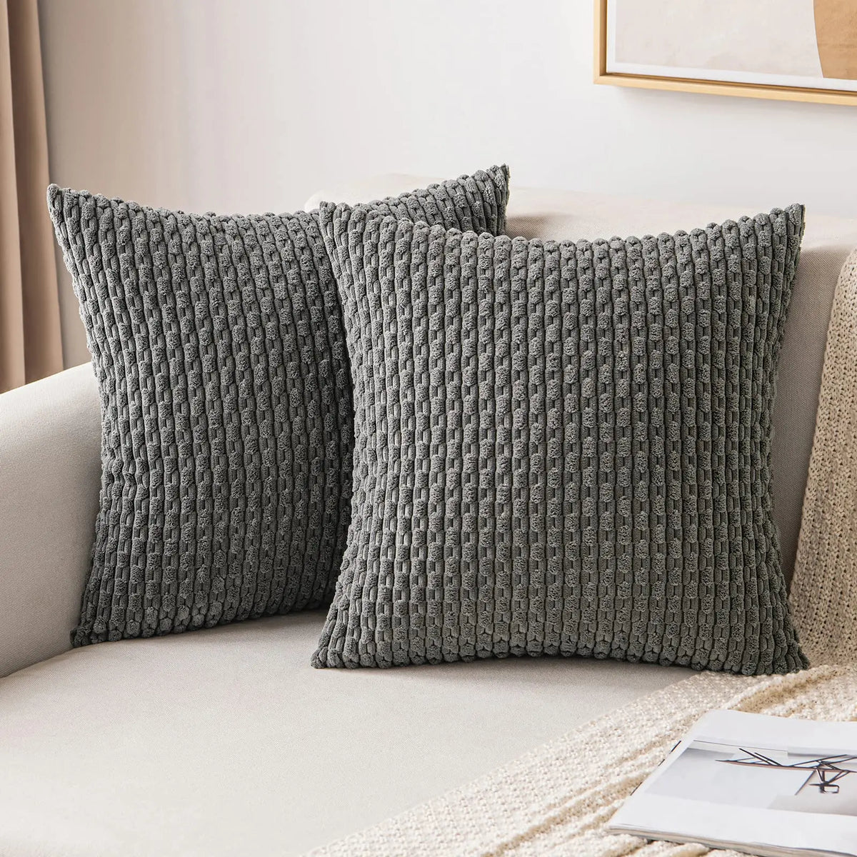 Two gray corduroy throw pillow covers with a textured weave resting on a light-colored sofa.