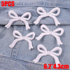 Five white embroidered bow iron-on patches placed on a denim fabric background.