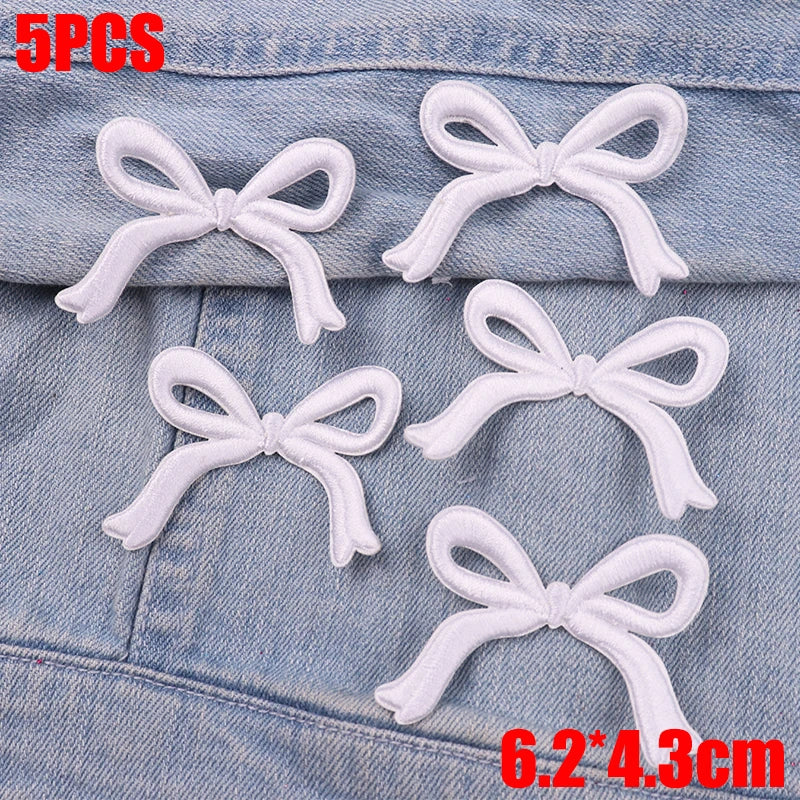 Five white embroidered bow iron-on patches placed on a denim fabric background.