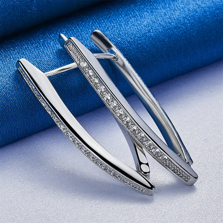 Par de aretes de aro plateados de ley en forma de V con detalles de zirconio, mostrados sobre tela azul.