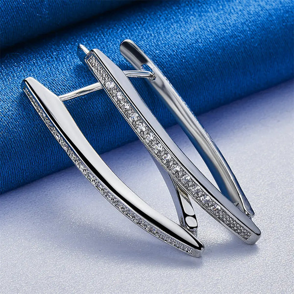 Pair of V-shaped sterling silver hoop earrings with zircon accents displayed on a blue fabric.