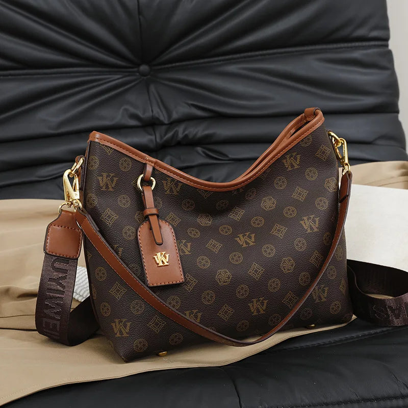 A brown leather tote bag with a monogram pattern rests on a black leather surface.