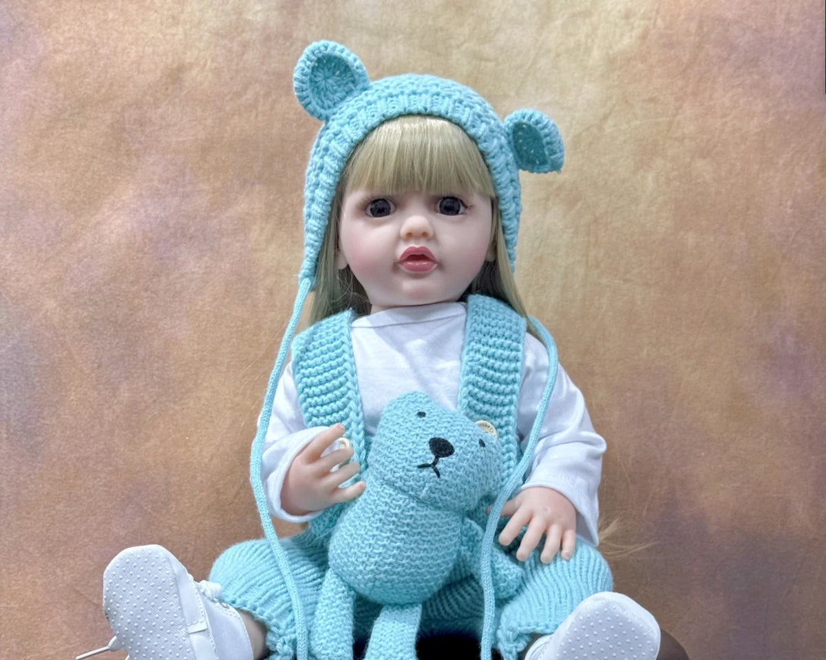 A baby doll wearing a light blue animal hood and holding a matching blue stuffed animal.