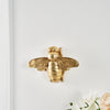 Golden bee-shaped resin wall decor mounted on a white wall.